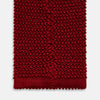 View 4 of product The Turnbull & Asser KNITTED RED SILK PLAIN TIE, featuring a textured finish, is rolled up and displayed against a plain white background.