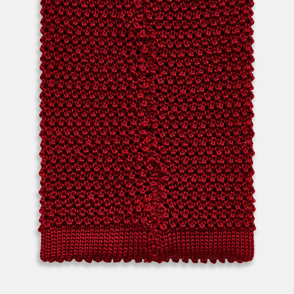 The Turnbull & Asser KNITTED RED SILK PLAIN TIE, featuring a textured finish, is rolled up and displayed against a plain white background.