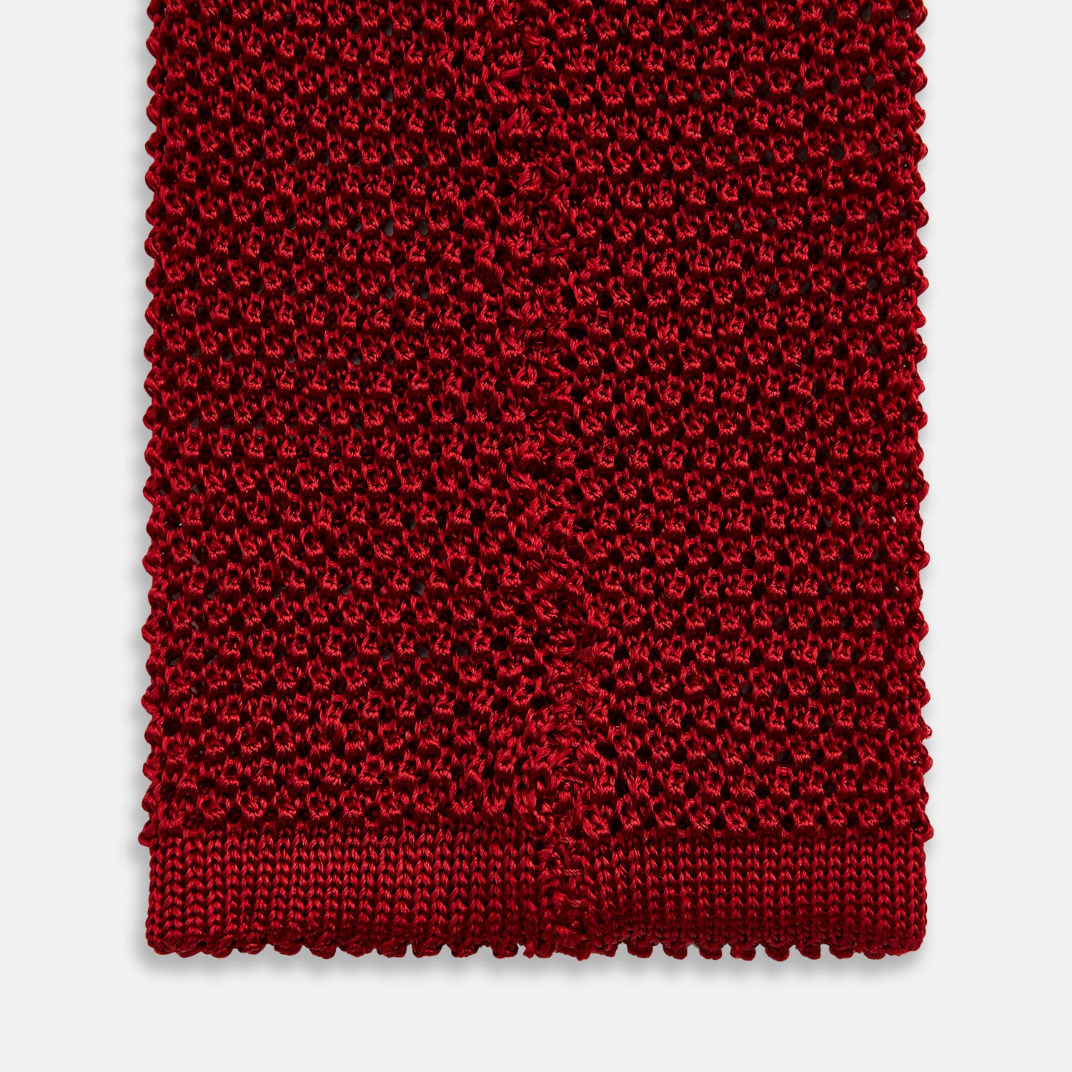 View 4 of product The Turnbull & Asser KNITTED RED SILK PLAIN TIE, featuring a textured finish, is rolled up and displayed against a plain white background.