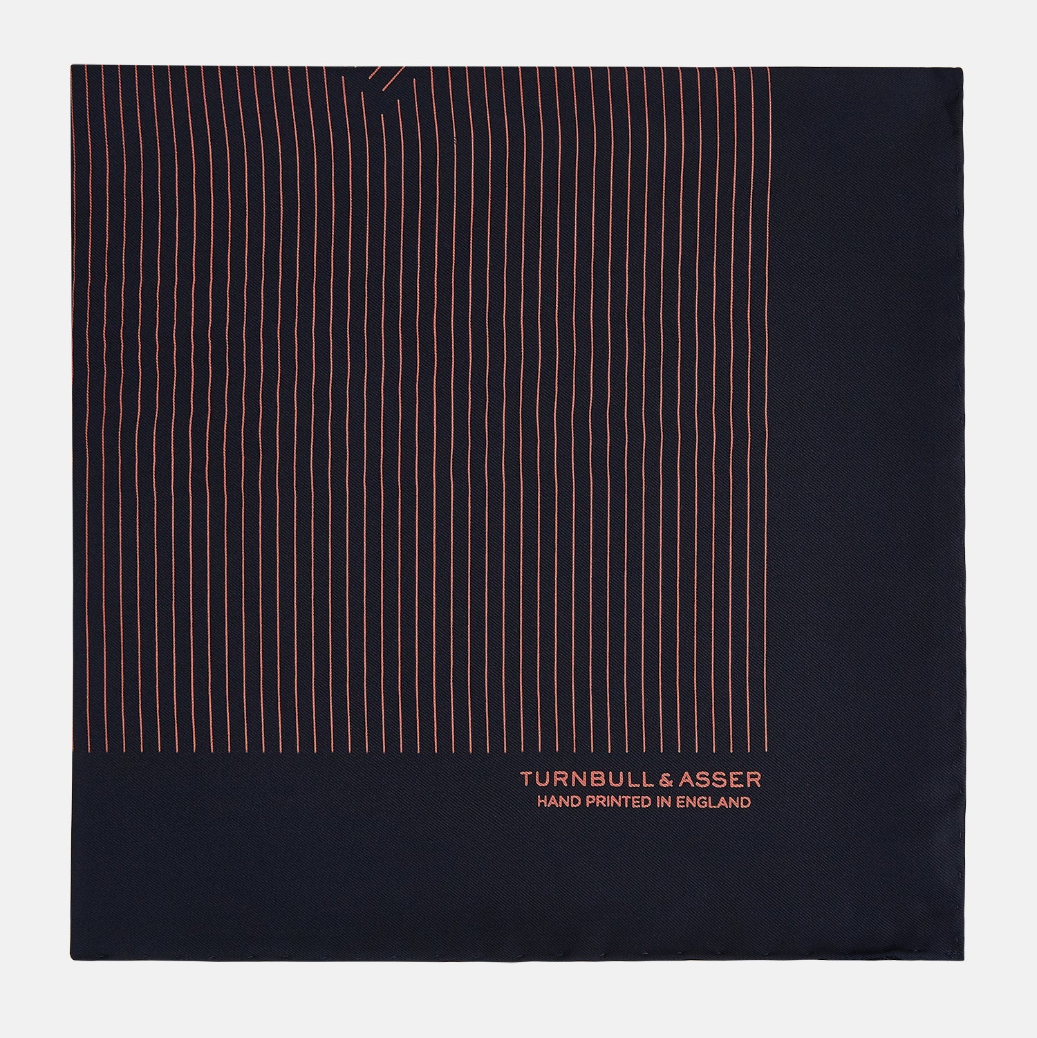 View 4 of product The Navy and Orange Stripe Silk Pocket Square by Turnbull & Asser is handmade in England from silk, featuring thin orange geometric stripes on navy and "Turnbull & Asser Hand Printed in England" printed in the corner.