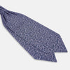 View 3 of product The Turnbull & Asser Lilac Paisley Silk Cravat showcases British elegance with its dark blue paisley pattern on a lilac background, beautifully displayed on a white surface.
