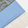 View 2 of product The Turnbull & Asser GGSC3128 5665 06 OS is a blue paisley silk scarf with ornate gold designs, solid light blue ends, and cream fringes. Shown laid flat with one end folded, it highlights its luxurious style.