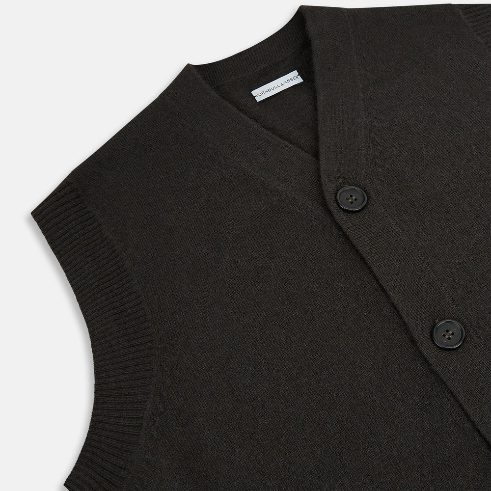 The Turnbull & Asser Dark Brown Cashmere Sleeveless Cardigan has a V-neck, button-up front, two front pockets, and ribbed trim on the armholes and hem, shown against a plain white background.