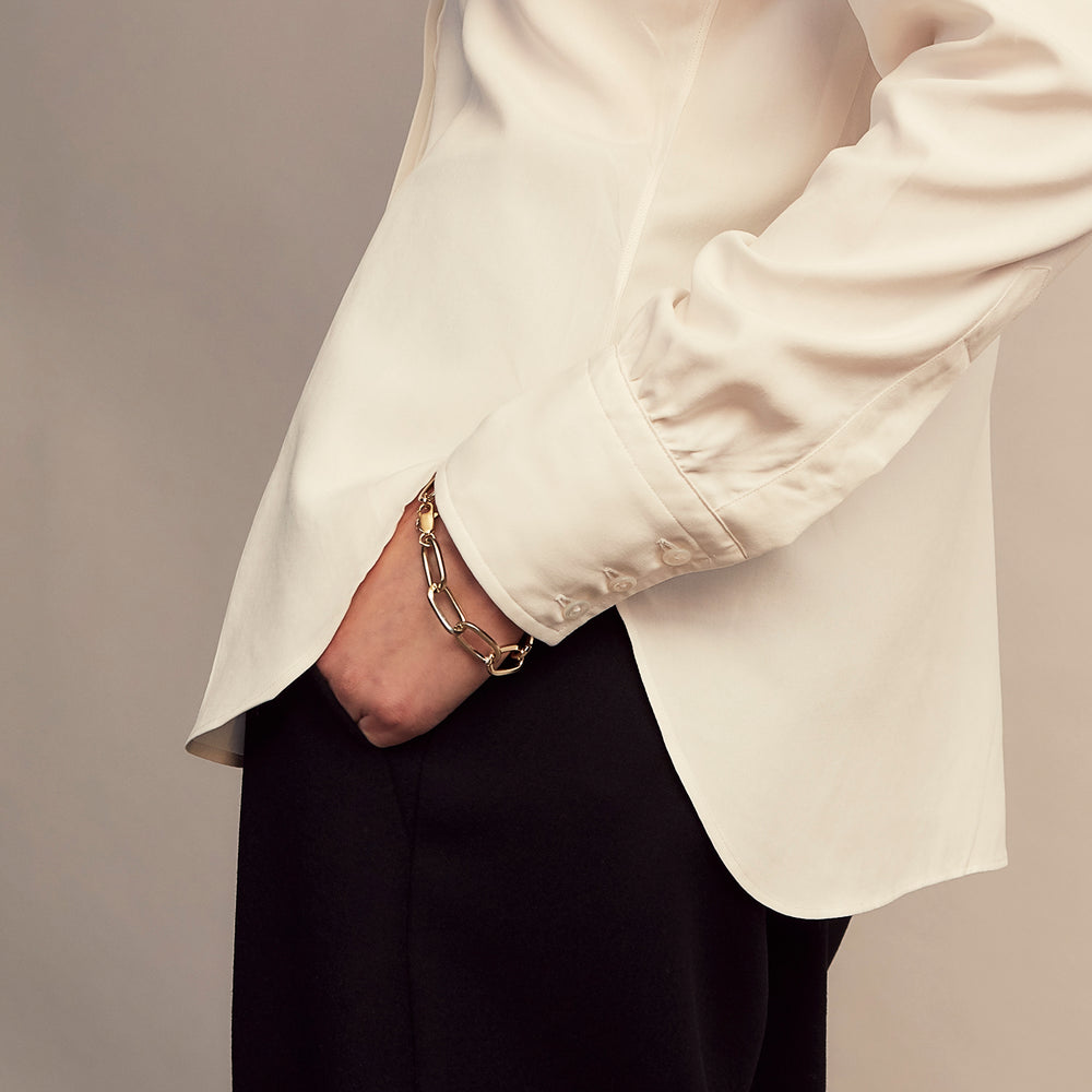 The Cream Silk Tailored Bianca Shirt by Turnbull & Asser features long sleeves, a pointed collar, and curved hem in soft-touch peace silk with a tailored fit. Shown laid flat on a white background.