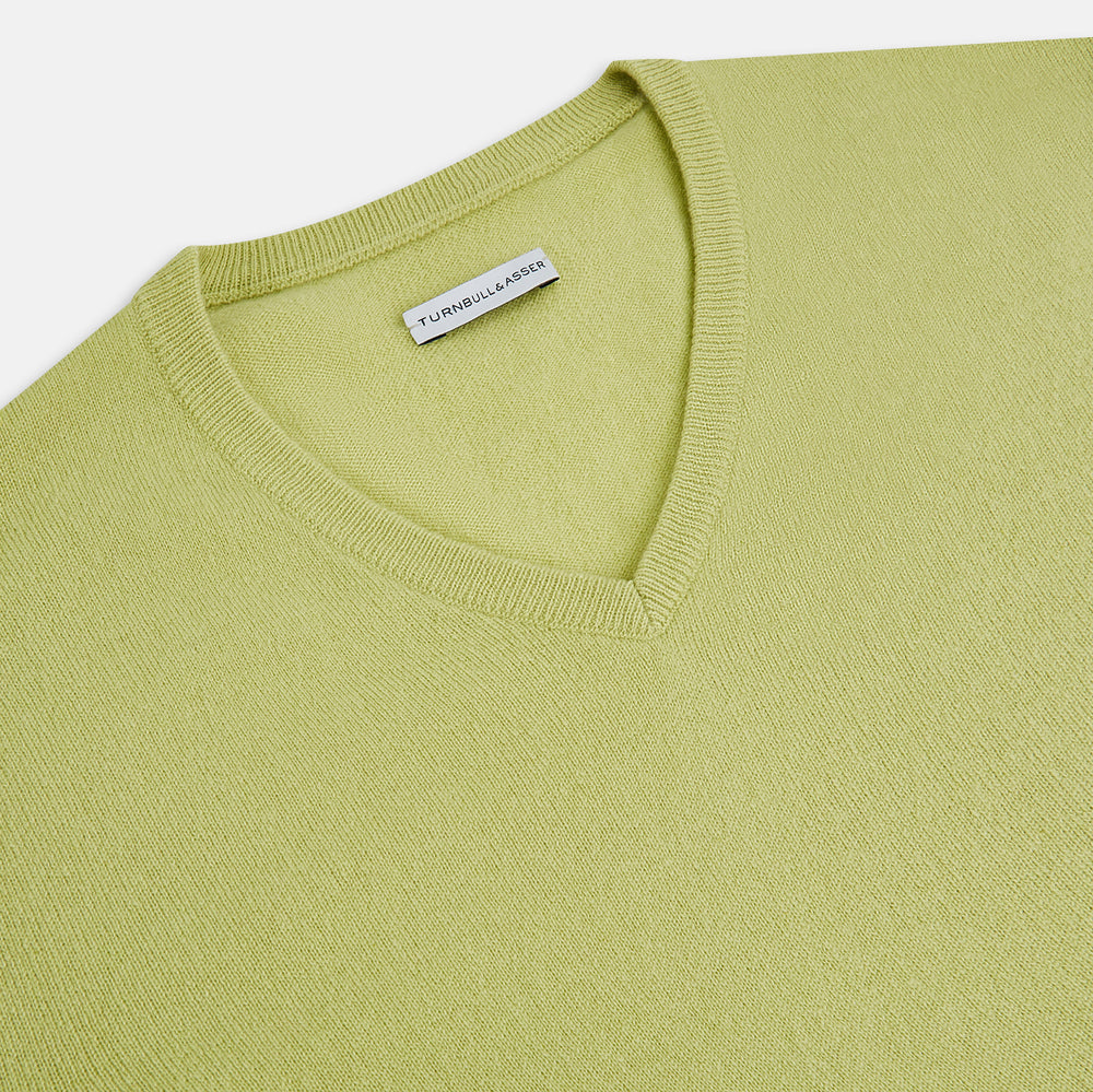 The Turnbull & Asser Melon Green Cashmere V-Neck Jumper features long sleeves with ribbed cuffs and hem, shown against a plain white background.