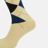 View 4 of product The Turnbull & Asser Vanilla Wool Check Mid-Length Sock is beige with blue, black, and white argyle diamonds on the side and solid beige toe, heel, and cuff. Displayed on a plain white background.