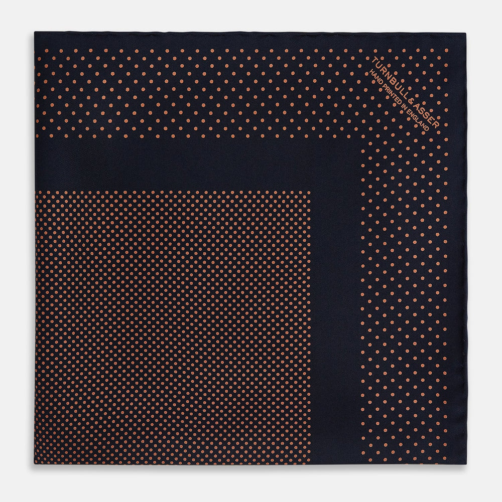 The Navy and Blush Dot Silk Pocket Square by Turnbull & Asser features a navy base with small orange polka dots and a border, shown neatly folded with one corner flipped over.