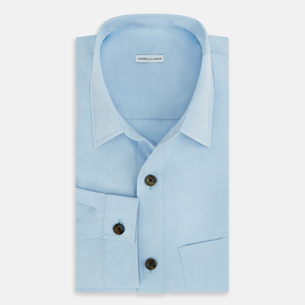 The Blue Hyde Overshirt by Turnbull & Asser features a light blue hue, long sleeves, a button-up front, and a single chest pocket. Crafted from sanforised cotton and shown laid flat on a white background.