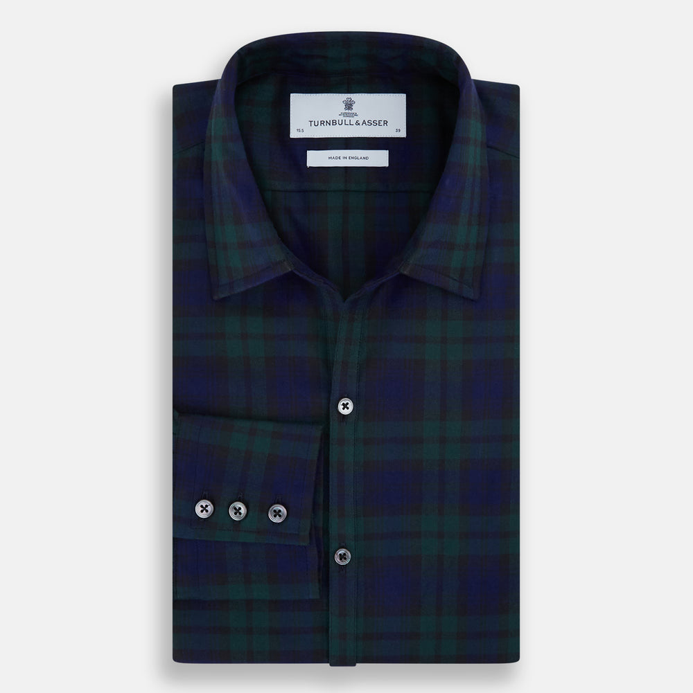 The Turnbull & Asser Black Watch Tartan Windsor Shirt is a long-sleeve, button-up shirt with a dark green and navy tartan pattern, white buttons, collar, and curved hem—showcasing British craftsmanship on a plain white background.