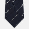 View 3 of product The Turnbull & Asser Navy Zigzag Jacquard Silk Tie is crafted from fine English silk, featuring a navy base with thin white zigzag stripes and shown rolled up on a plain white background.