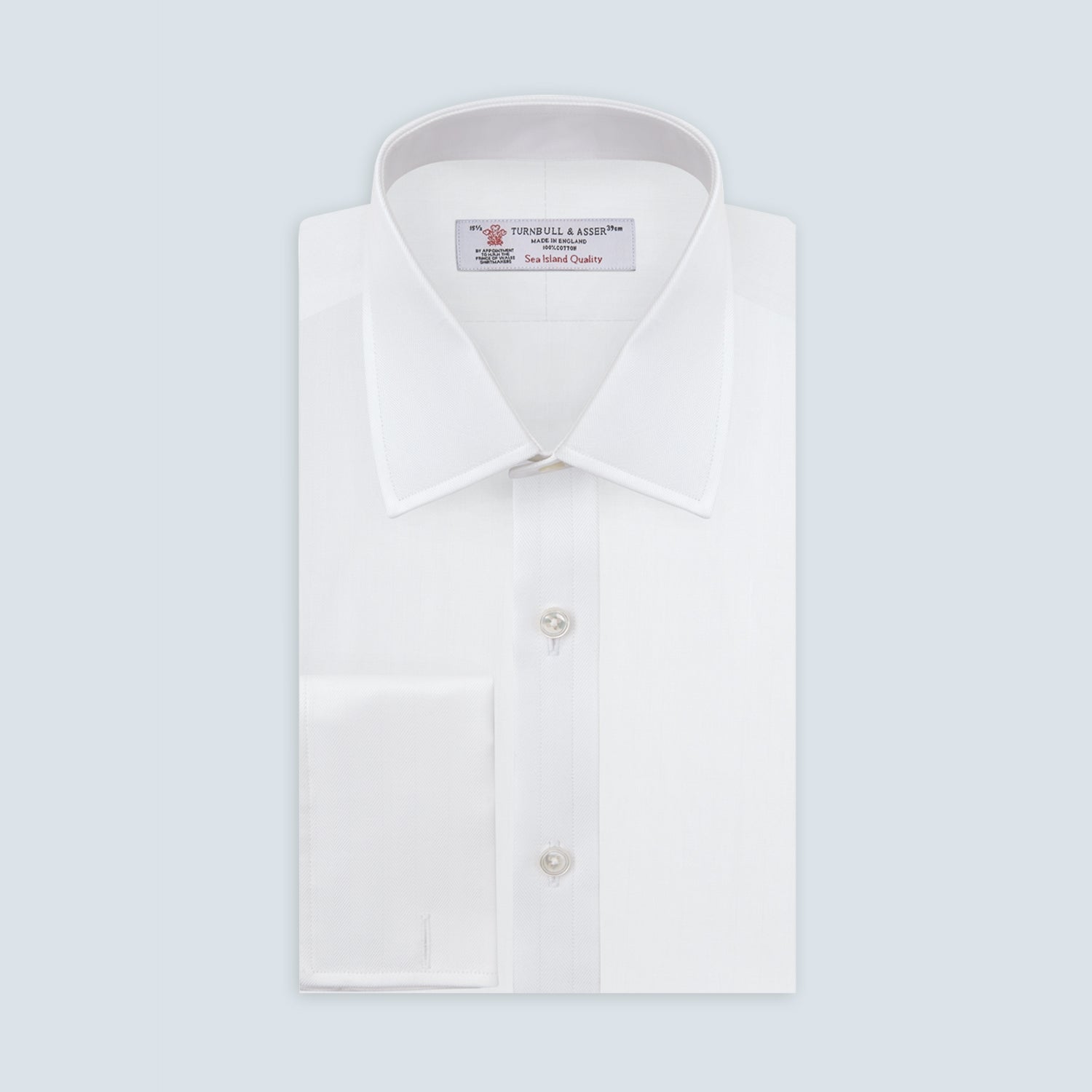 View 1 of product The Turnbull & Asser White Herringbone Sea Island Quality Cotton Shirt features a T&A collar, double cuffs, and chest pocket. Crafted for luxury with a classic design, it’s shown neatly folded against a light grey background—ideal for evening wear.