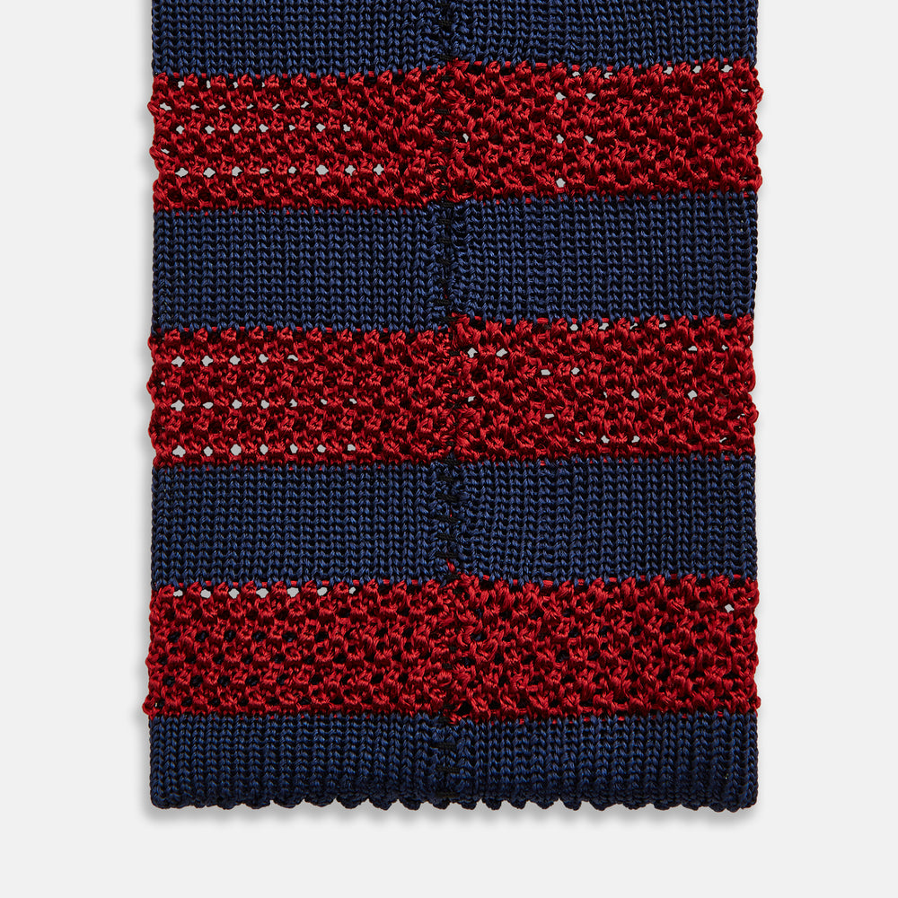 The Turnbull & Asser KNITTED STRIPE RED TIE features bold red and navy wide stripes in a rolled-up, knitted design—an eye-catching accessory shown on a plain white background.