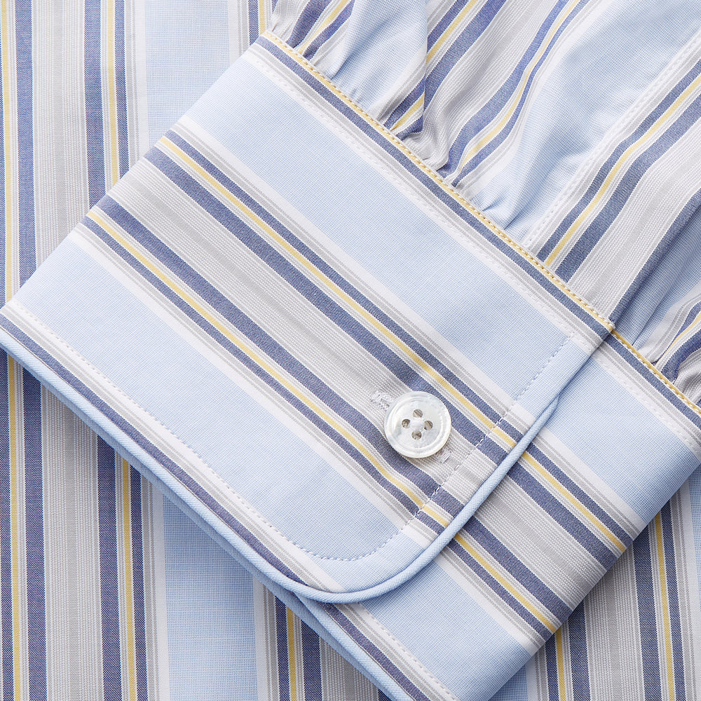 The Pale Blue and Yellow Multi Stripe Cotton Sussex Nightshirt by Turnbull & Asser features long sleeves, a knee-length cut, a collar, button-down front, chest pocket, and rounded hem.