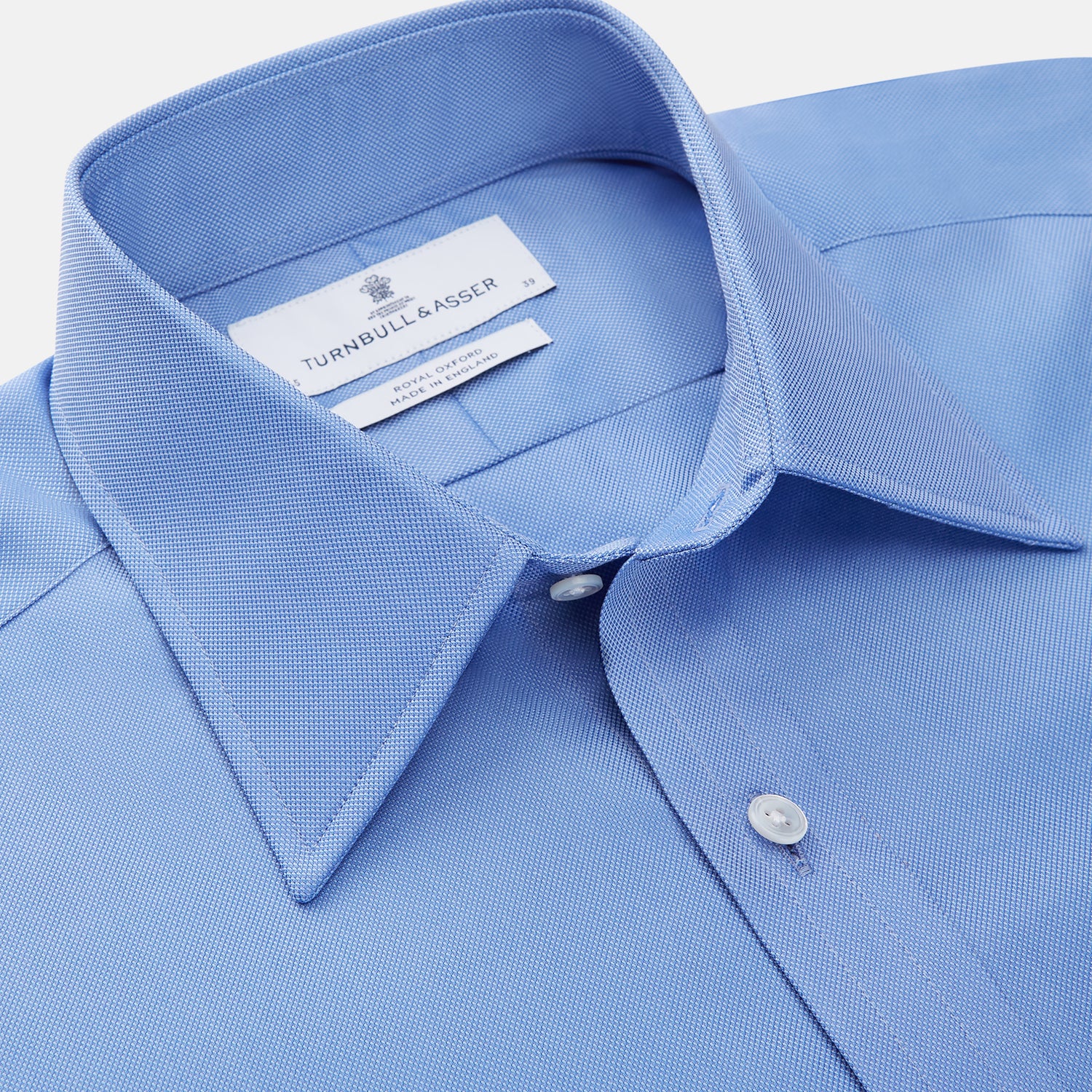 View 3 of product The Turnbull & Asser "The World Is Not Enough" blue cotton Istanbul shirt, as seen on James Bond, is a light blue oxford long-sleeve button-up with a pointed collar and white buttons, displayed on a white background.