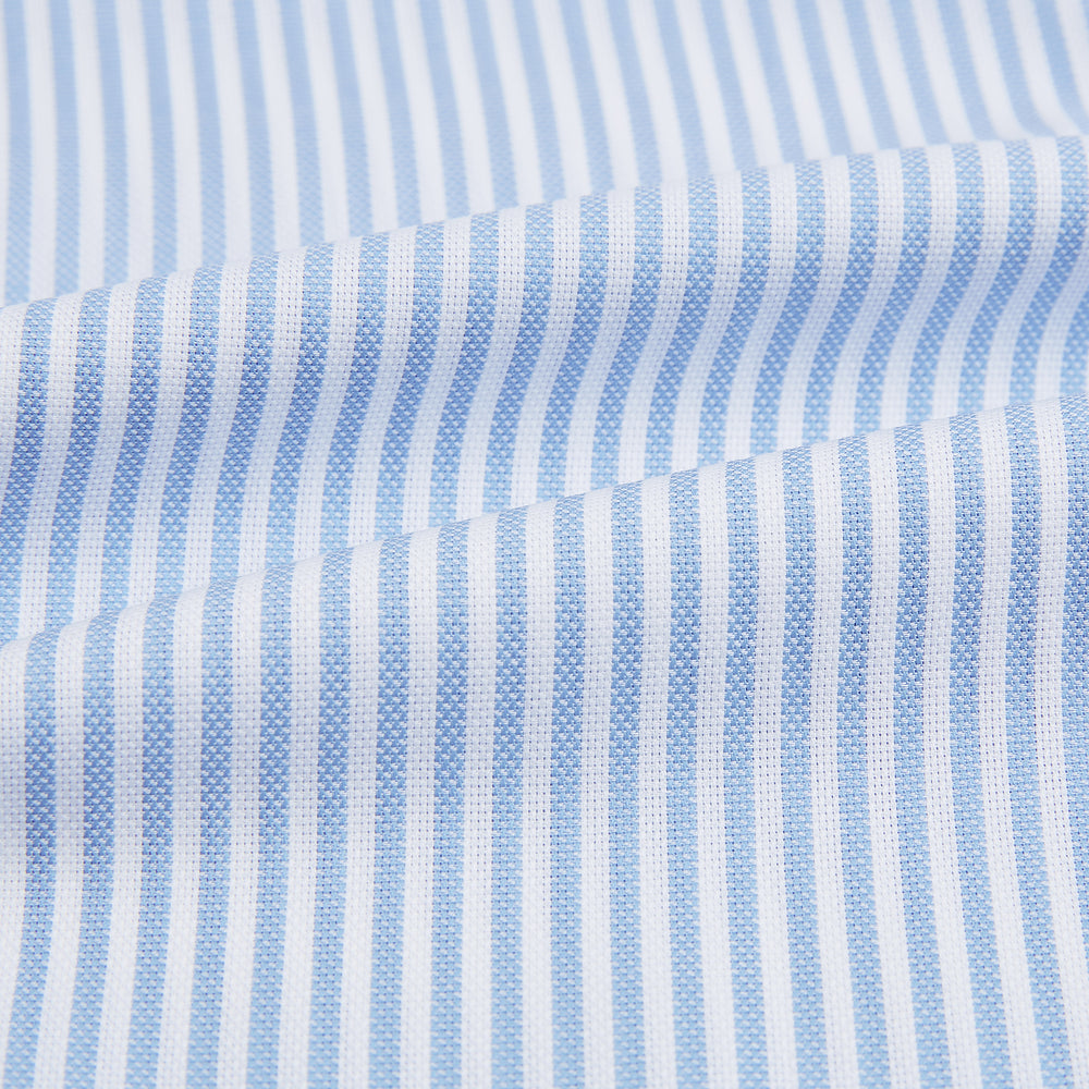 The Turnbull & Asser Blue Bengal Stripe Mayfair Shirt features light blue and white vertical stripes, a classic T&A collar, white buttons, and buttoned cuffs. Laid flat on a white background.