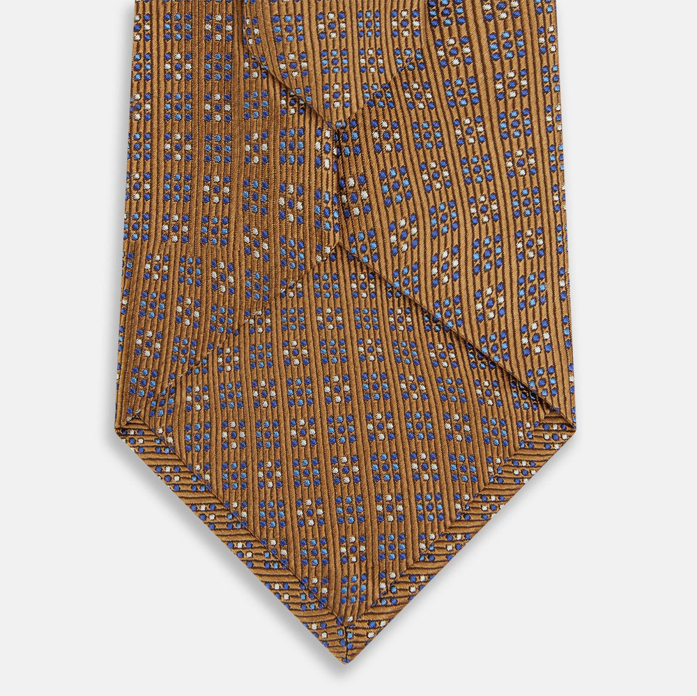 The Turnbull & Asser Tan and Blue Multi Dot Silk Tie is rolled up, showcasing a refined dotted pattern on silk—an elegant accessory ideal for elevating modern office attire.