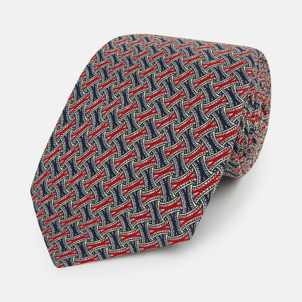 A close-up of the Turnbull & Asser Red and Navy Weave Patterned Silk Tie, showcasing its geometric design in red, blue, white, and yellow on a white background.