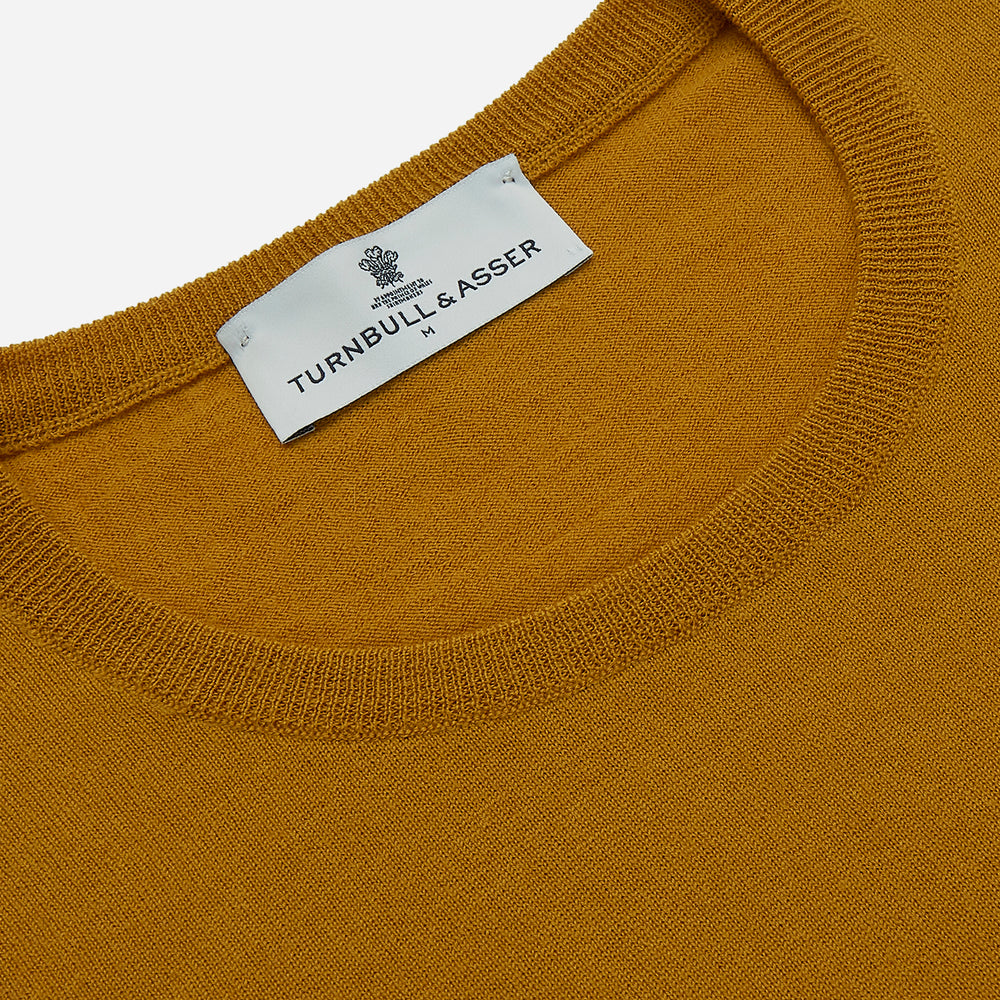 The Turnbull & Asser Gold Crew Neck Merino Jumper, featuring long sleeves and ribbed cuffs and hem, is displayed flat on a white background.