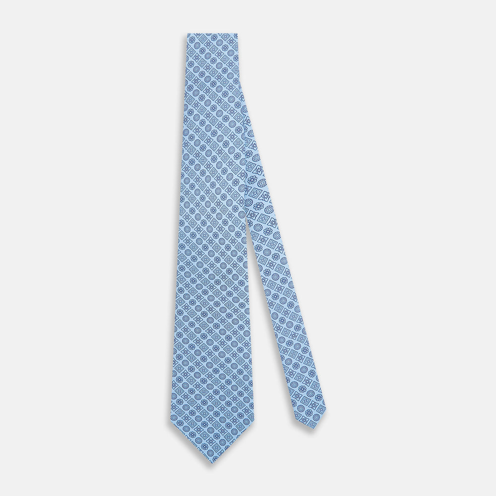 The Turnbull & Asser Blue Floral Tile Pattern Printed Silk Tie features a light blue geometric and floral design in dark blue, shown rolled up on a white background.