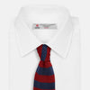 View 2 of product The Turnbull & Asser KNITTED STRIPE RED TIE features bold red and navy wide stripes in a rolled-up, knitted design—an eye-catching accessory shown on a plain white background.