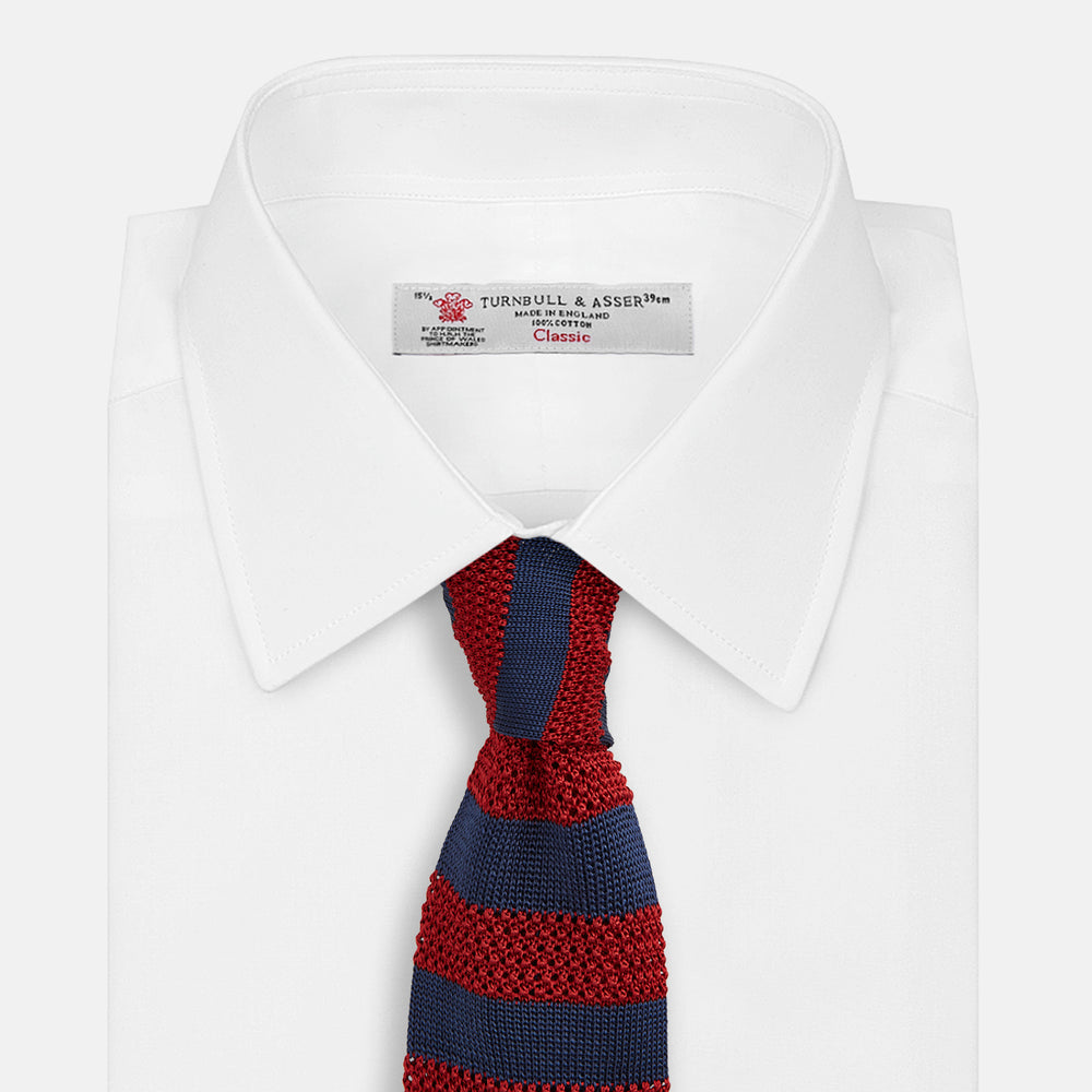 The Turnbull & Asser KNITTED STRIPE RED TIE features bold red and navy wide stripes in a rolled-up, knitted design—an eye-catching accessory shown on a plain white background.