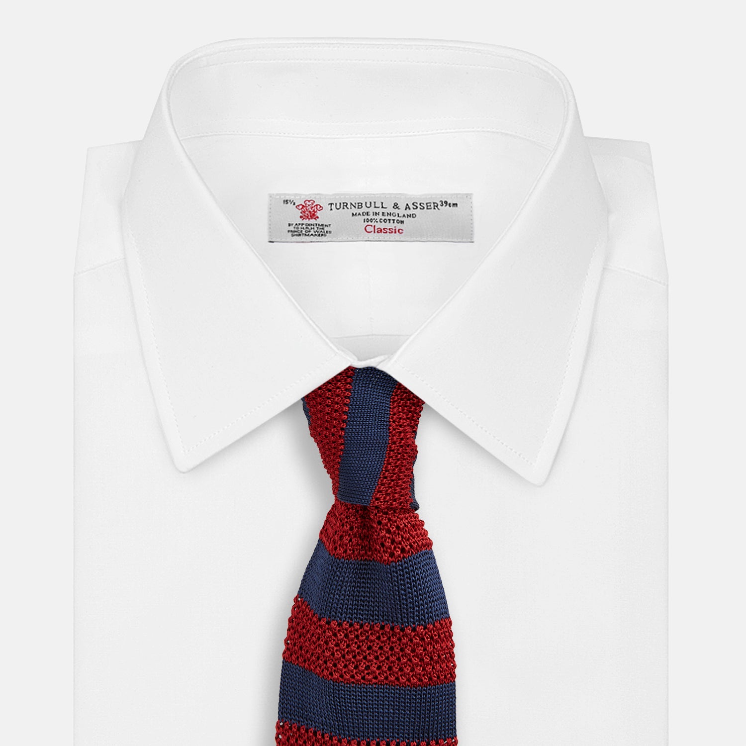 View 2 of product The Turnbull & Asser KNITTED STRIPE RED TIE features bold red and navy wide stripes in a rolled-up, knitted design—an eye-catching accessory shown on a plain white background.