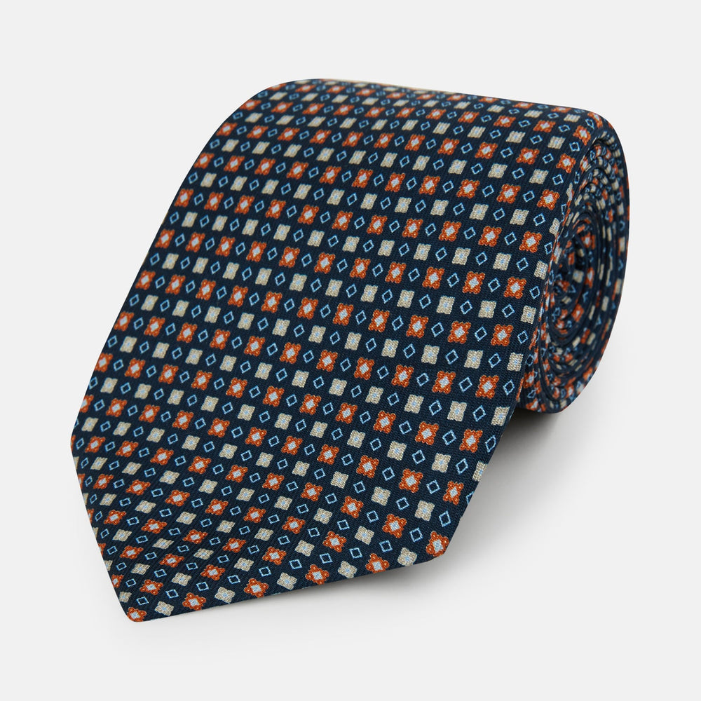 The Turnbull & Asser Navy and Orange Geometric Motif Silk Tie features a dark blue base with small orange, white, and light blue geometric patterns—a refined statement of British craftsmanship.
