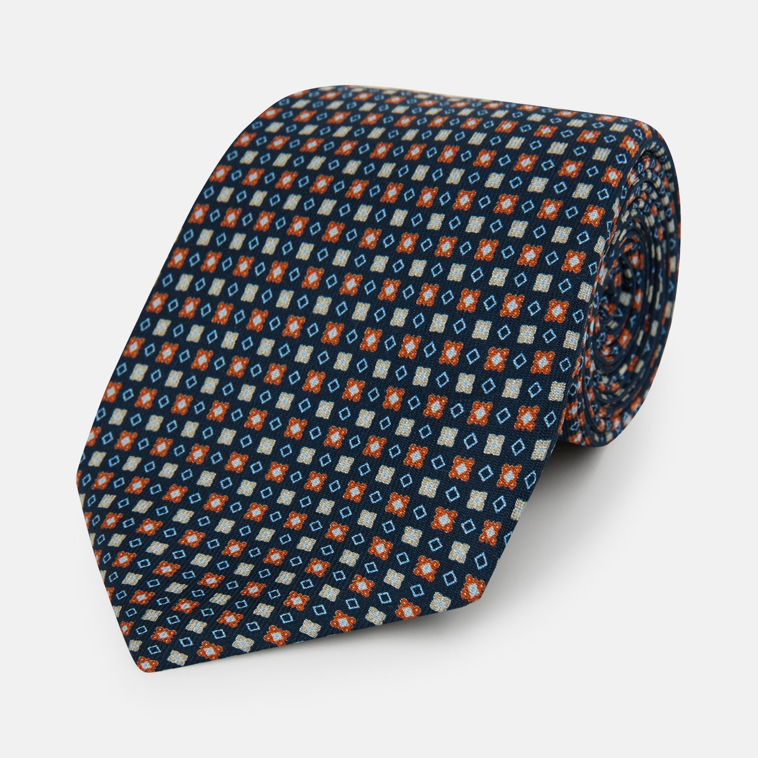 View 1 of product The Turnbull & Asser Navy and Orange Geometric Motif Silk Tie features a dark blue base with small orange, white, and light blue geometric patterns—a refined statement of British craftsmanship.