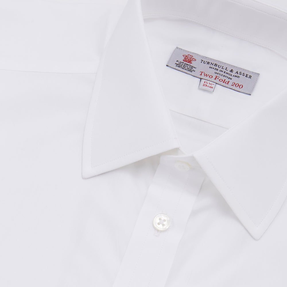 A Turnbull & Asser Two-Fold 200 White Cotton Shirt with T&A collar and double cuffs, neatly folded to show the label inside the collar, is displayed on a light blue background.