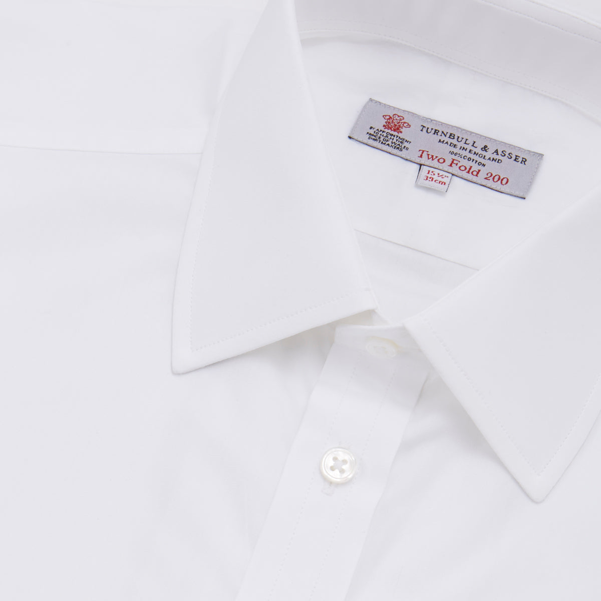 View 5 of product A Turnbull & Asser Two-Fold 200 White Cotton Shirt with T&A collar and double cuffs, neatly folded to show the label inside the collar, is displayed on a light blue background.