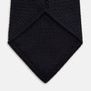 View 4 of product The GRENADINE NAVY TIE by Turnbull & Asser—a rolled, dark navy blue textured tie—serves as an essential accessory for smart outfits, shown against a plain white background.