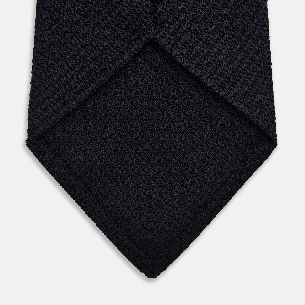 The GRENADINE NAVY TIE by Turnbull & Asser—a rolled, dark navy blue textured tie—serves as an essential accessory for smart outfits, shown against a plain white background.