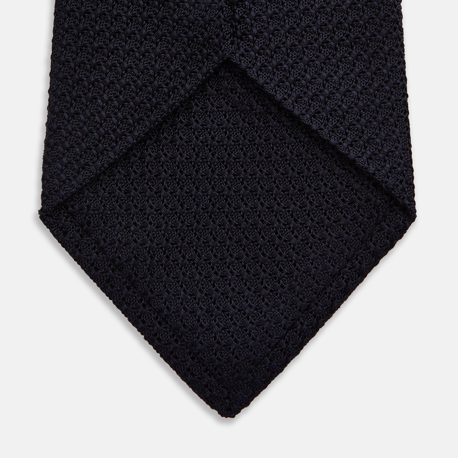 View 4 of product The GRENADINE NAVY TIE by Turnbull & Asser—a rolled, dark navy blue textured tie—serves as an essential accessory for smart outfits, shown against a plain white background.