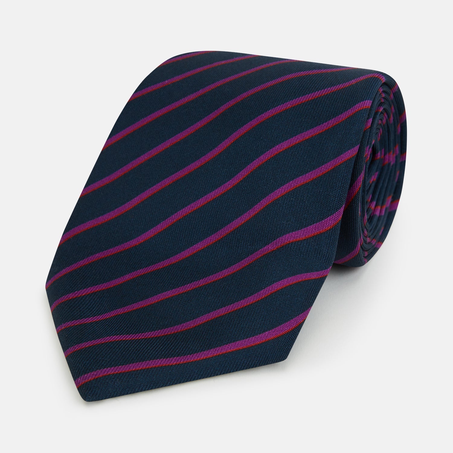 View 1 of product The Turnbull & Asser Navy and Purple Striped Blazer Silk Tie features British craftsmanship with diagonal magenta and purple stripes, displayed neatly rolled on a white background.