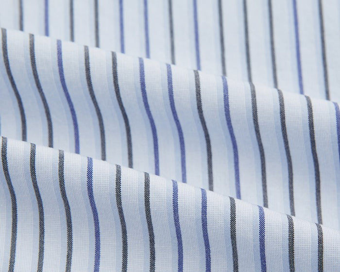 Close-up of white fabric with evenly spaced blue, black, and grey vertical stripes, shown with gentle folds.