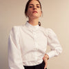 View 8 of product A woman stands in profile, looking down with hands in her pockets, wearing the Turnbull & Asser Turnbull and The Deck White Cotton Expressionist Shirt, paired with high-waisted black-and-white houndstooth pants.