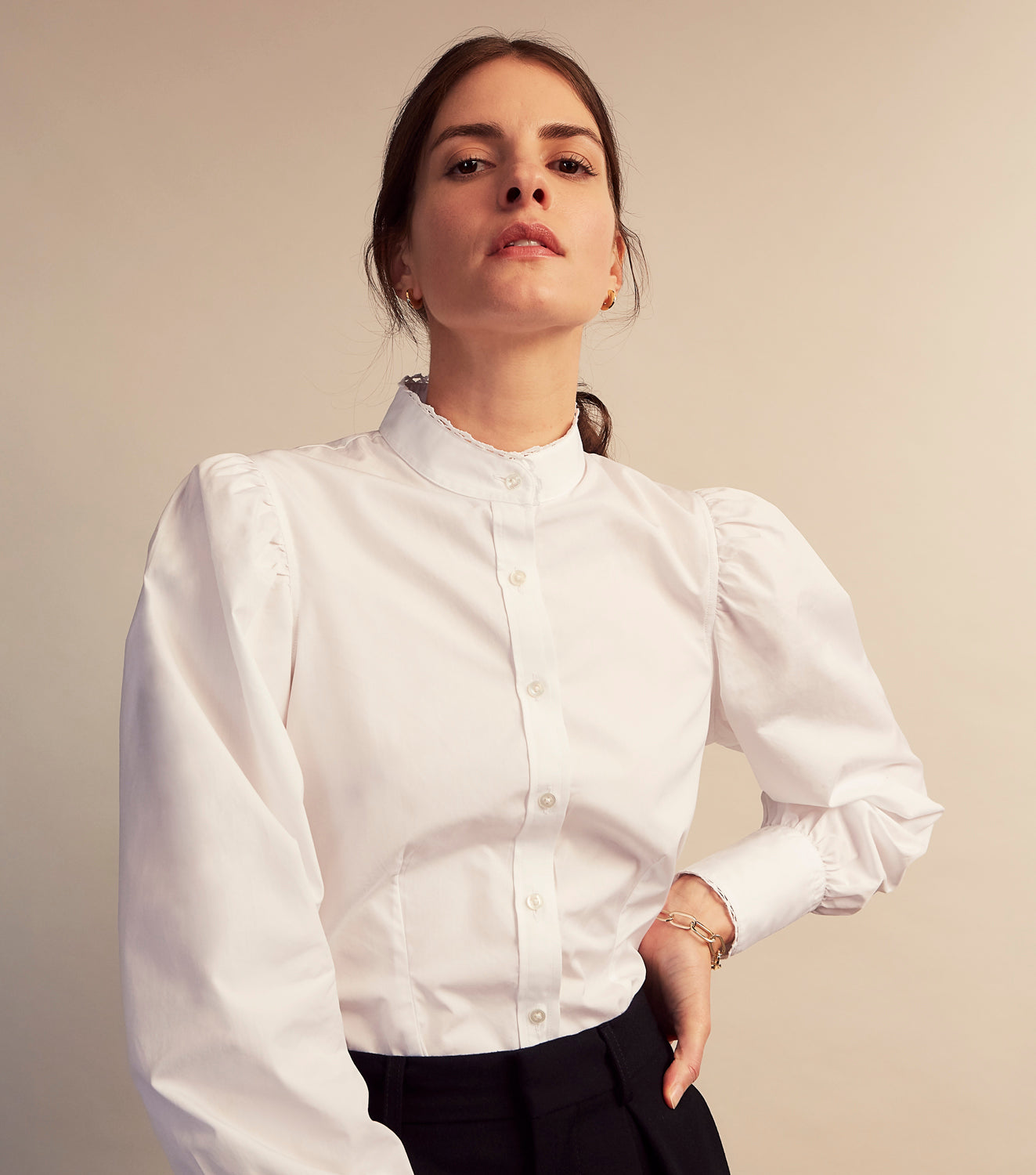 View 8 of product A woman stands in profile, looking down with hands in her pockets, wearing the Turnbull & Asser Turnbull and The Deck White Cotton Expressionist Shirt, paired with high-waisted black-and-white houndstooth pants.