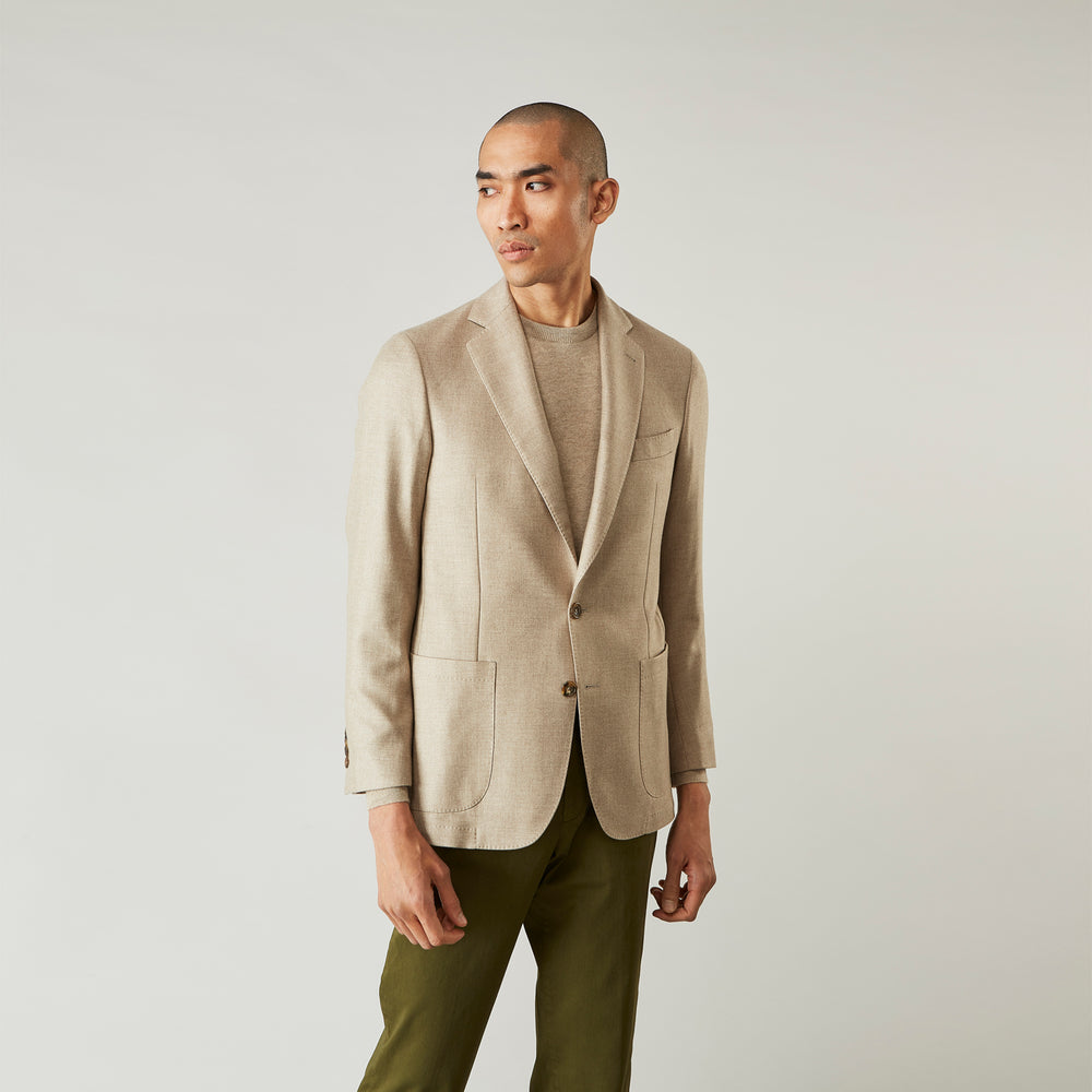 A man wearing the Beige Wool, Silk and Cashmere Bern Jacket by Turnbull & Asser over a matching shirt and olive green pants stands against a plain light gray background, looking to his left with a neutral expression.