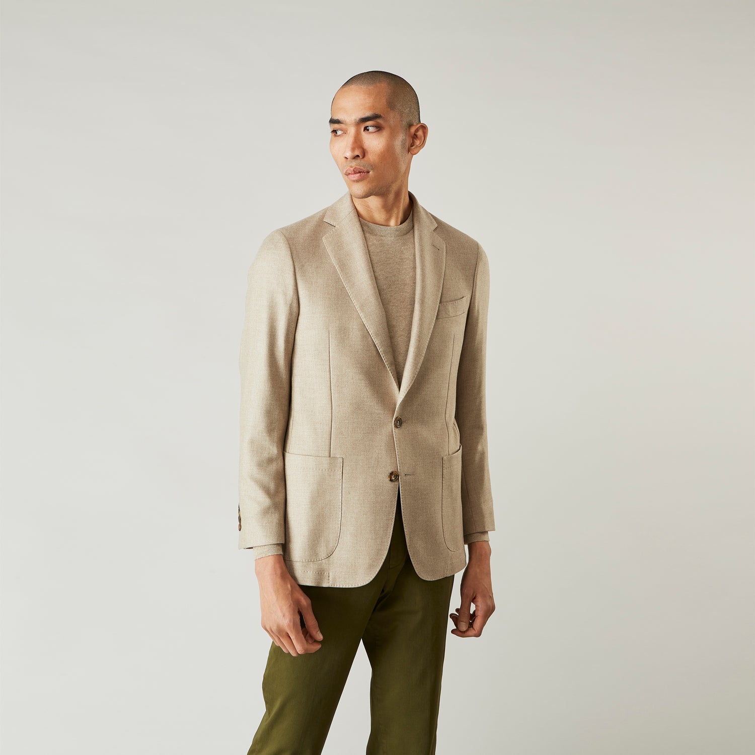 View 1 of product A man wearing the Beige Wool, Silk and Cashmere Bern Jacket by Turnbull & Asser over a matching shirt and olive green pants stands against a plain light gray background, looking to his left with a neutral expression.
