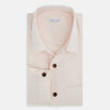 View 5 of product The Turnbull & Asser Pale Pink Hyde Overshirt is a long-sleeve, sanforised cotton button-up with a left chest pocket and dark buttons, shown laid flat on a white background.