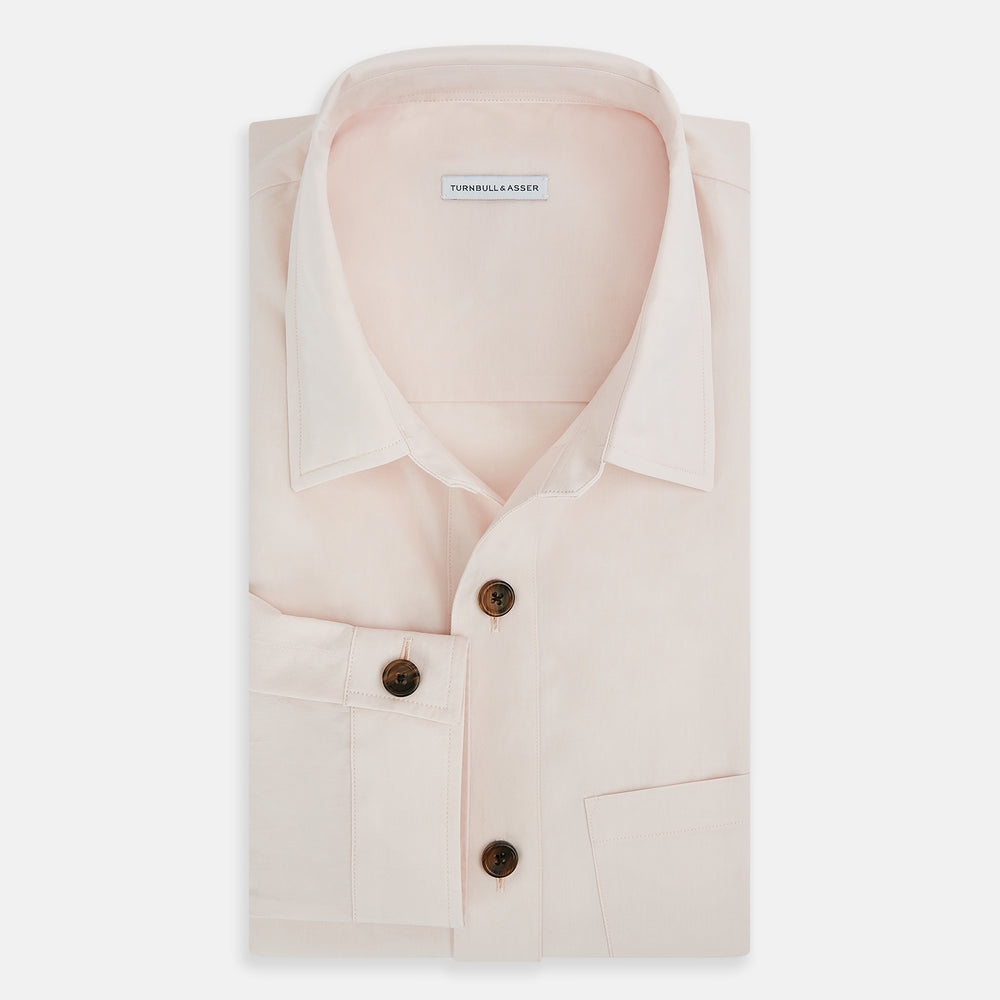 The Turnbull & Asser Pale Pink Hyde Overshirt is a long-sleeve, sanforised cotton button-up with a left chest pocket and dark buttons, shown laid flat on a white background.