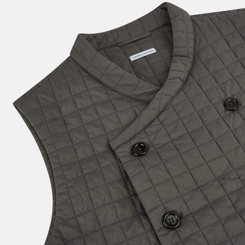 The Turnbull & Asser Shadow Grey Double-Breasted Quilted Gilet features a sleeveless design, asymmetrical collar, side zip pockets, slanted chest pocket, grid pattern, and modern black buttons—perfect for layered dressing.