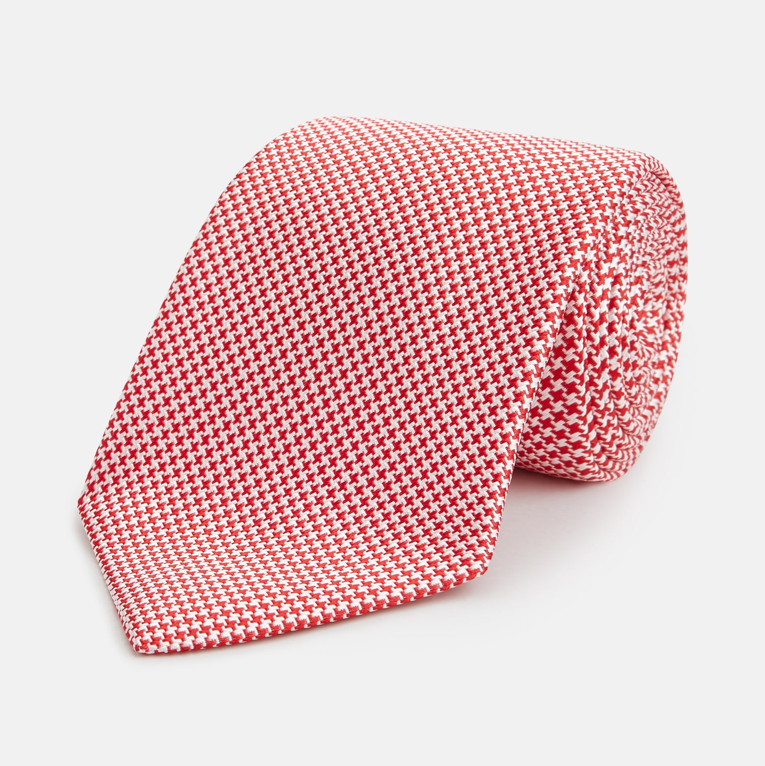 View 1 of product The Turnbull & Asser Red Houndstooth Silk Tie features a textured, small geometric pattern in red and white—ideal as a classic office accessory, shown rolled up on a plain white background.