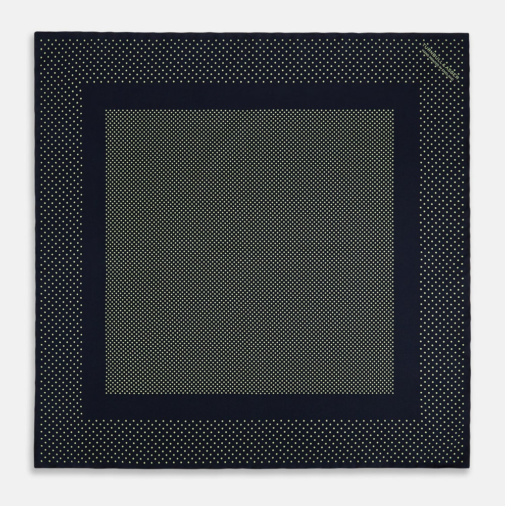 The Turnbull & Asser Navy and Melon Green Dot Silk Pocket Square features small melon green dots on navy silk with a solid border. One corner is folded over to highlight its exquisite handmade craftsmanship.