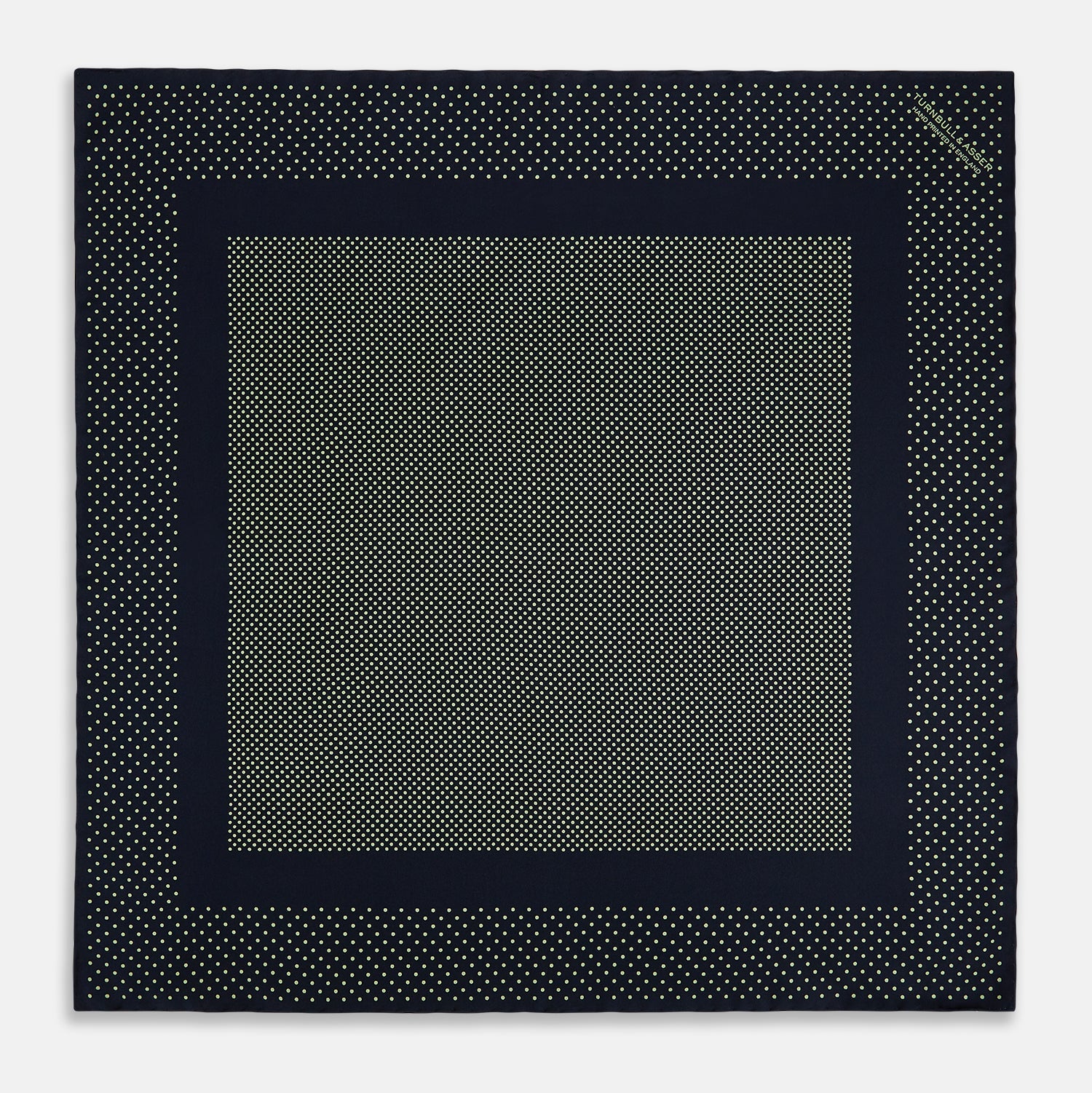 View 4 of product The Turnbull & Asser Navy and Melon Green Dot Silk Pocket Square features small melon green dots on navy silk with a solid border. One corner is folded over to highlight its exquisite handmade craftsmanship.