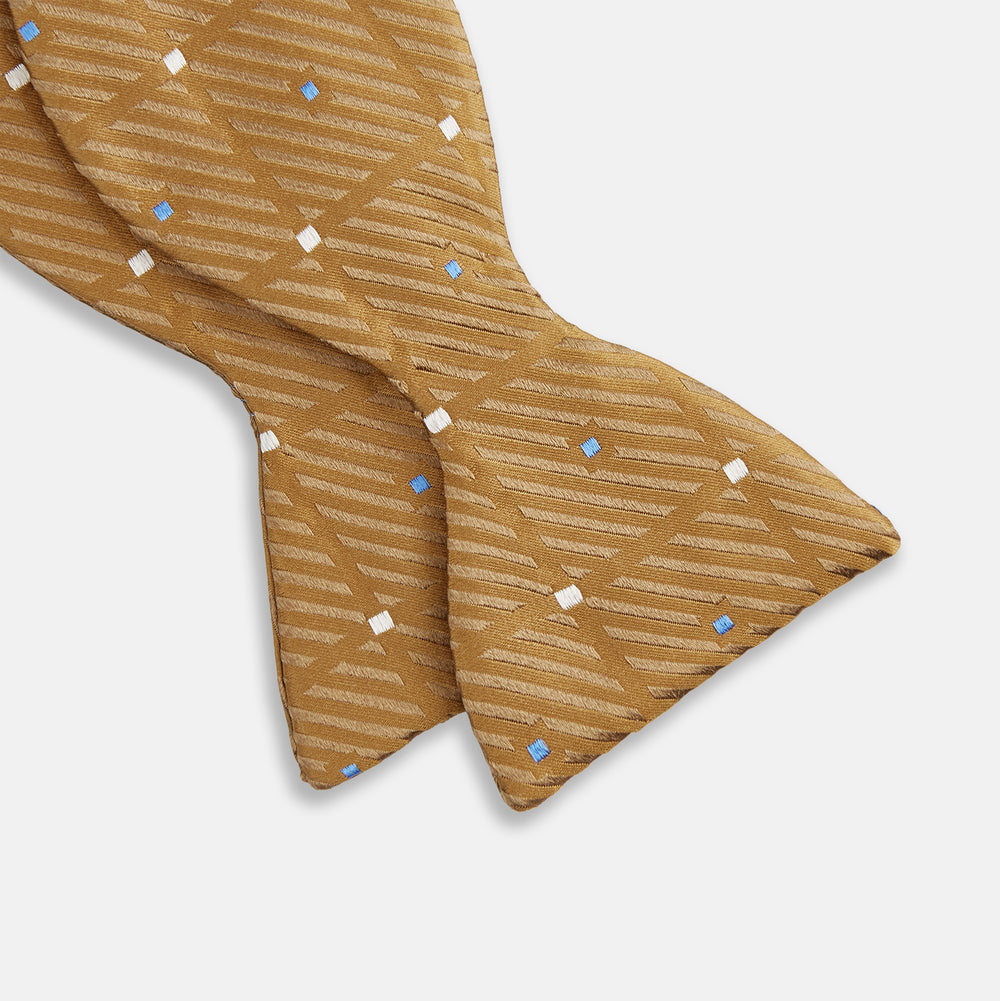 The Thistle Petersham Double End Bow Tie by Turnbull & Asser features a golden brown hue with a subtle diagonal stripe and blue and white square accents—an elegant accessory, pictured on a plain white background.