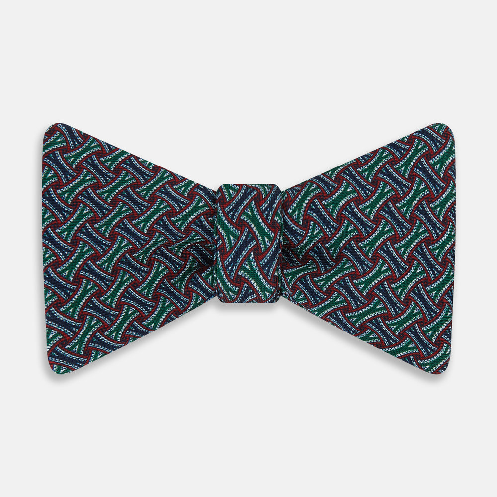 The Forest Green and Red Weave Patterned Silk Bow Tie by Turnbull & Asser features interwoven red, blue, and forest green lines with white dotted accents in a geometric design on a dark background.