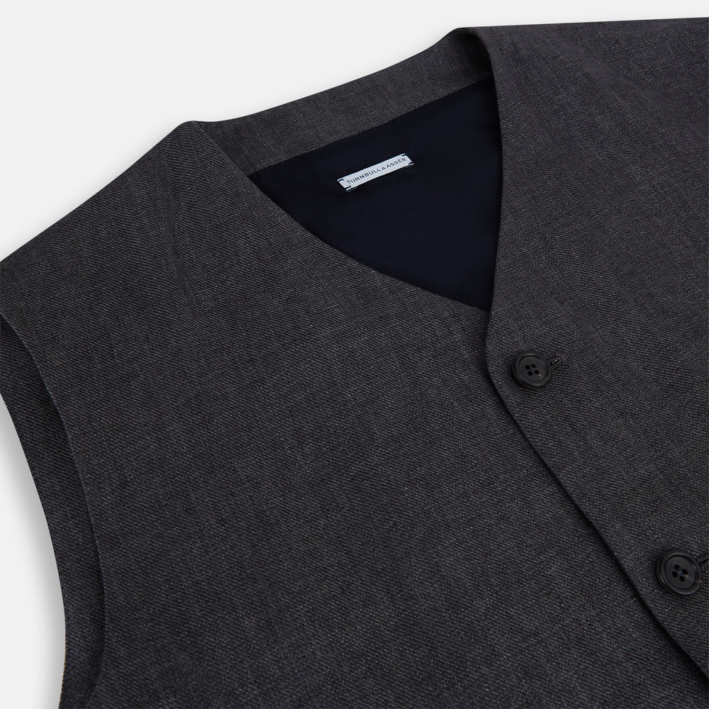 The Turnbull & Asser Ash Linen Twill Waistcoat is a dark gray, sleeveless V-neck with three front buttons, a chest pocket, and two diagonal zippered pockets in subtly textured twill. Shown on a plain white background.