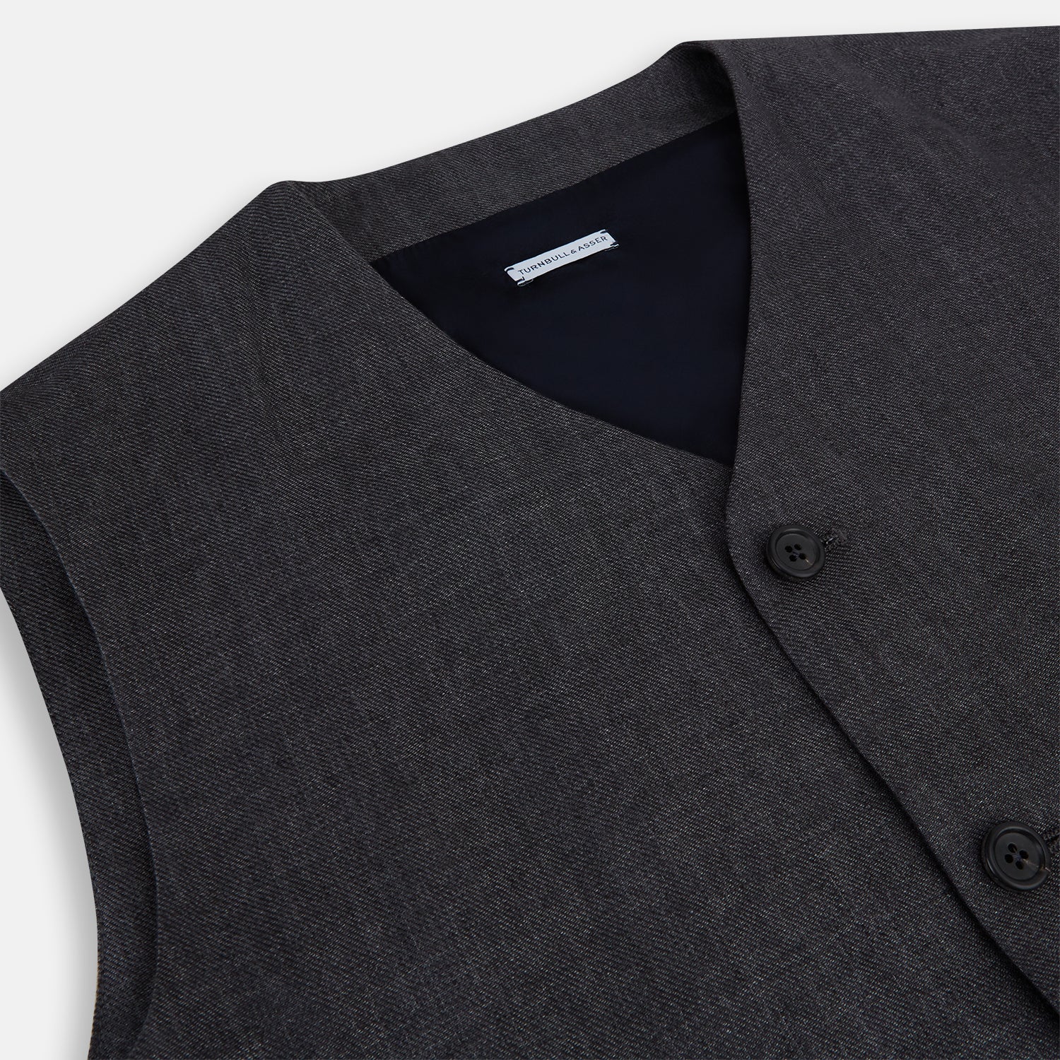 View 2 of product The Turnbull & Asser Ash Linen Twill Waistcoat is a dark gray, sleeveless V-neck with three front buttons, a chest pocket, and two diagonal zippered pockets in subtly textured twill. Shown on a plain white background.