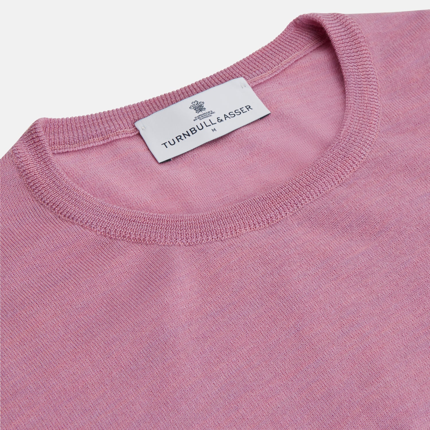 View 3 of product Wearing Turnbull & Asser’s Pink Merino Kingston Crew Neck Jumper, white pants, and a colorful scarf, a person stands against a plain light gray background with hands in their pockets.